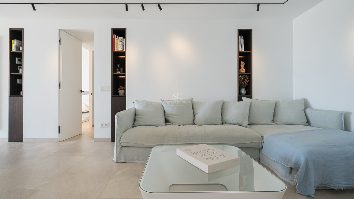 Salon moderne avec canapé vert sauge, table en verre et niches murales en bois sombre.