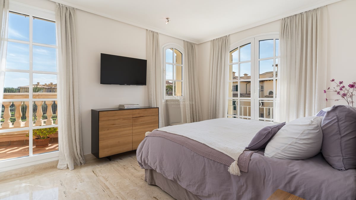 Chambre élégante avec lit parme, sol en travertin, grandes fenêtres cintrées et accès au balcon.