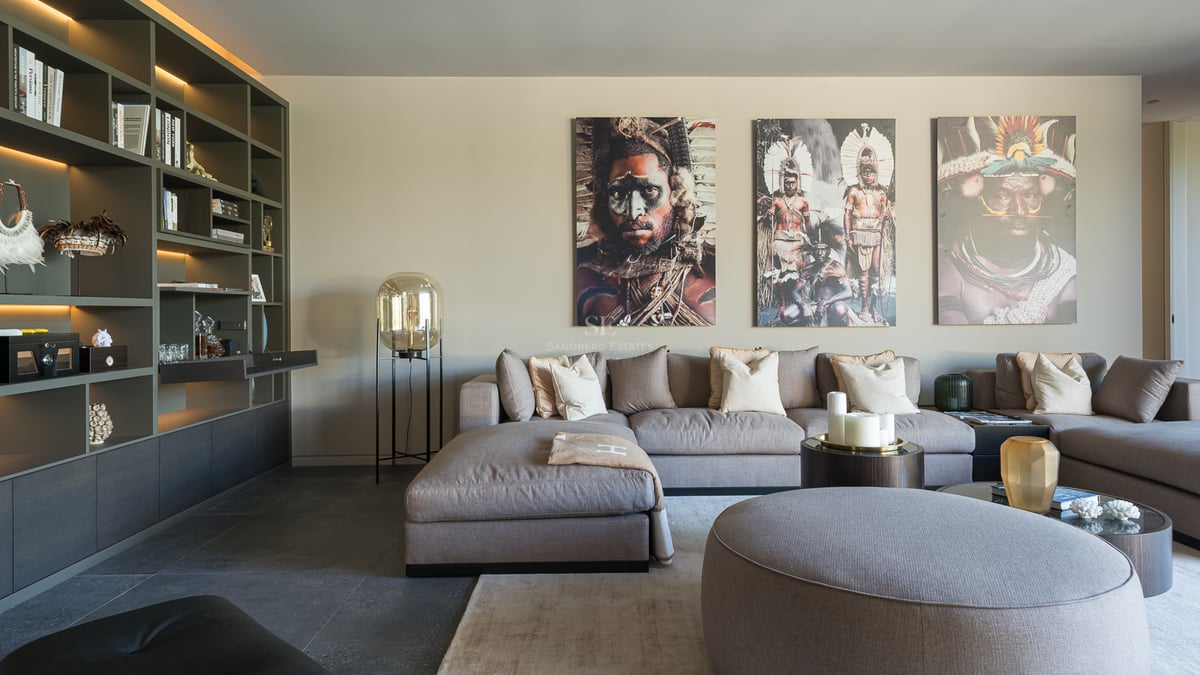 Salon moderne avec un grand canapé modulaire gris, une bibliothèque intégrée et trois portraits tribaux au mur.