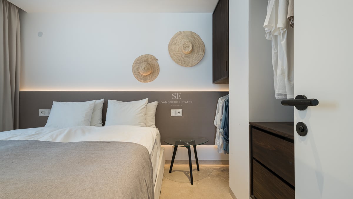 Chambre moderne avec tête de lit rétroéclairée, draps blancs et chapeaux de paille décoratifs au mur.