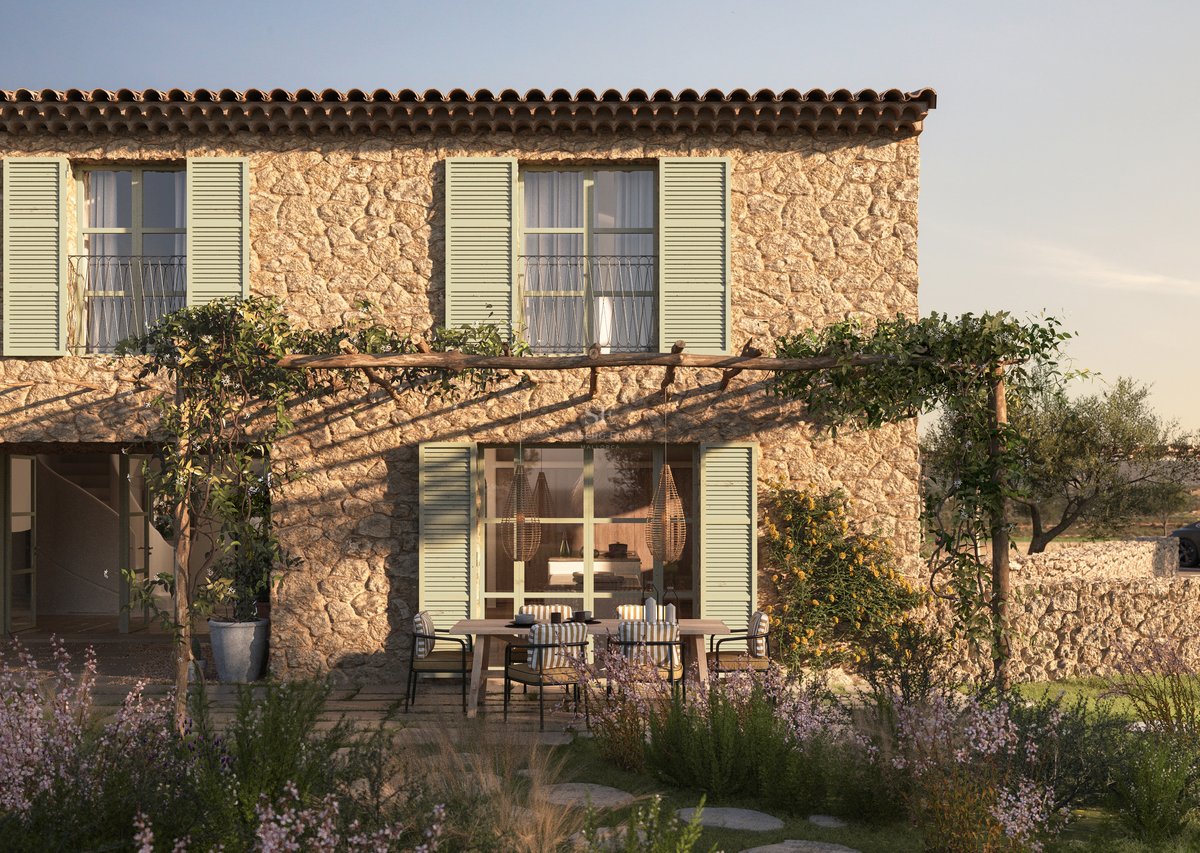 Façade en pierre avec volets vert sauge et pergola rustique surplombant un coin repas extérieur dans un jardin.