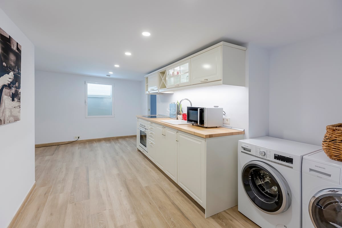 Cuisine moderne lumineuse avec placards blancs, plans de travail en bois clair et lave-linge et sèche-linge intégrés.