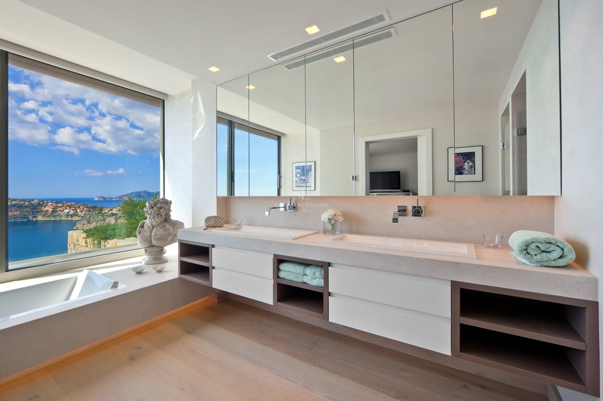 Salle de bain moderne avec double vasque et grande baie vitrée offrant une vue panoramique sur la mer.