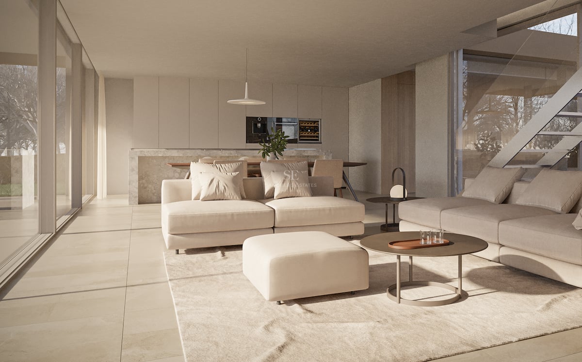 Salon moderne avec canapé crème, pouf et table basse ronde s'ouvrant sur une salle à manger épurée.