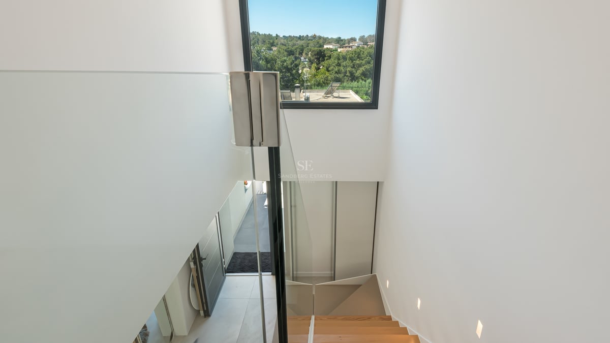 Vue intérieure d'un escalier en chêne avec garde-corps en verre donnant sur un paysage méditerranéen verdoyant.