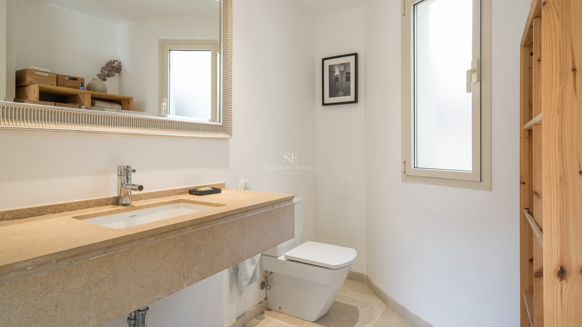 Salle de bain lumineuse avec vasque en pierre beige, grand miroir au cadre argenté, toilettes blanches et fenêtre dépolie.