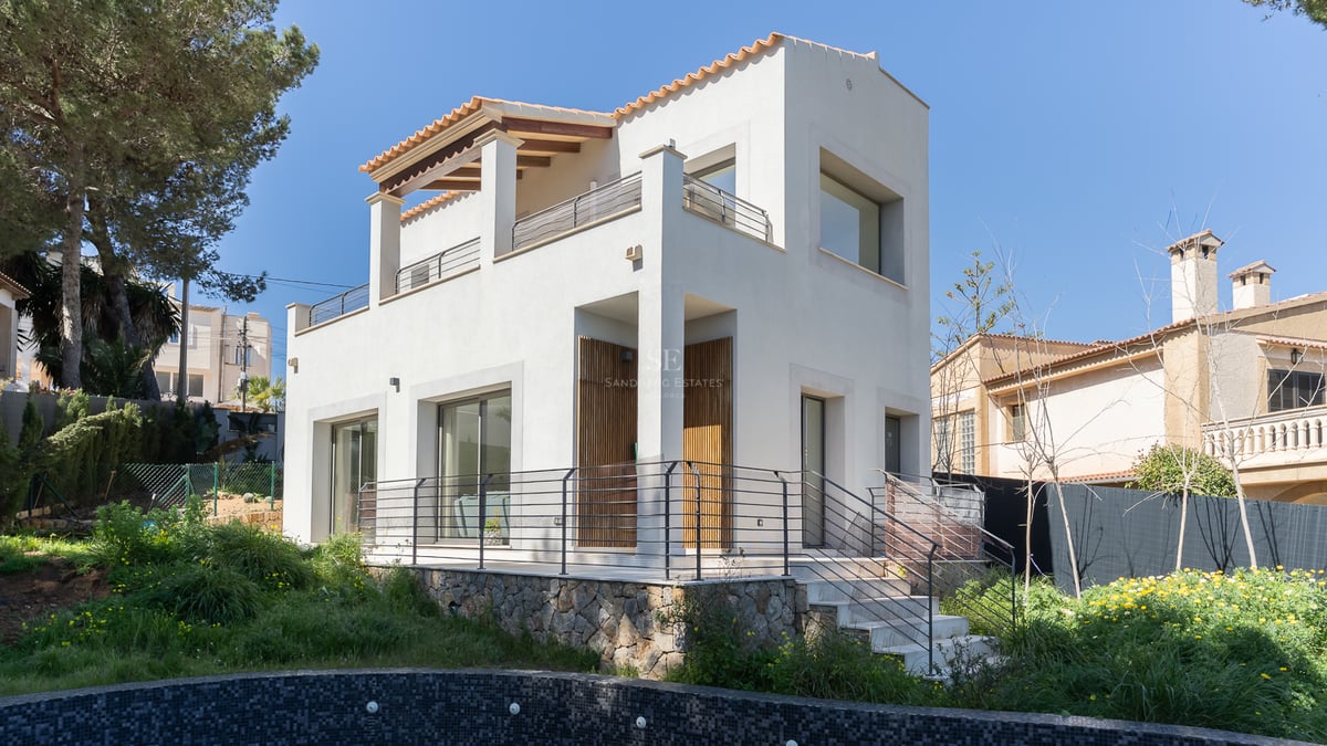 Villa moderne blanche de deux étages avec base en pierre naturelle et toit en terre cuite sous un ciel dégagé.