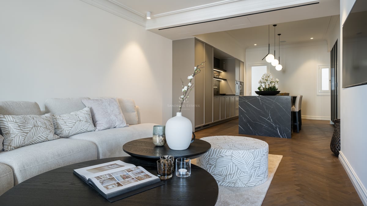 A contemporary open-plan living room and kitchen featuring herringbone floors, a dark marble island, and neutral furnishings.