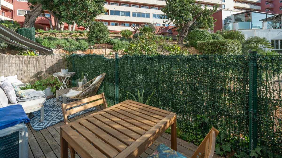 Terrasse ensoleillée avec table à manger en bois, coin détente et clôture de confidentialité verdoyante.