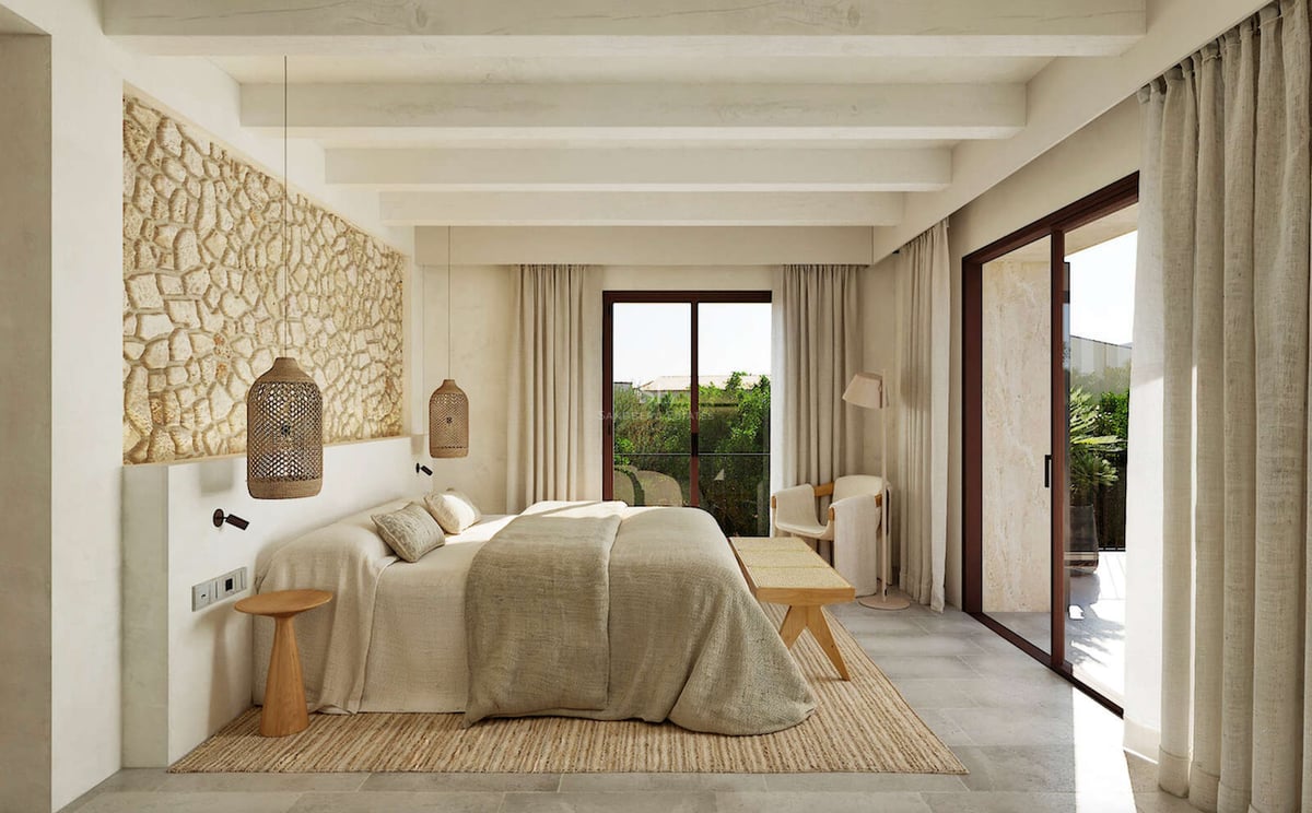 Chambre de luxe avec mur en pierre apparente, poutres en bois et baies vitrées donnant sur le jardin.