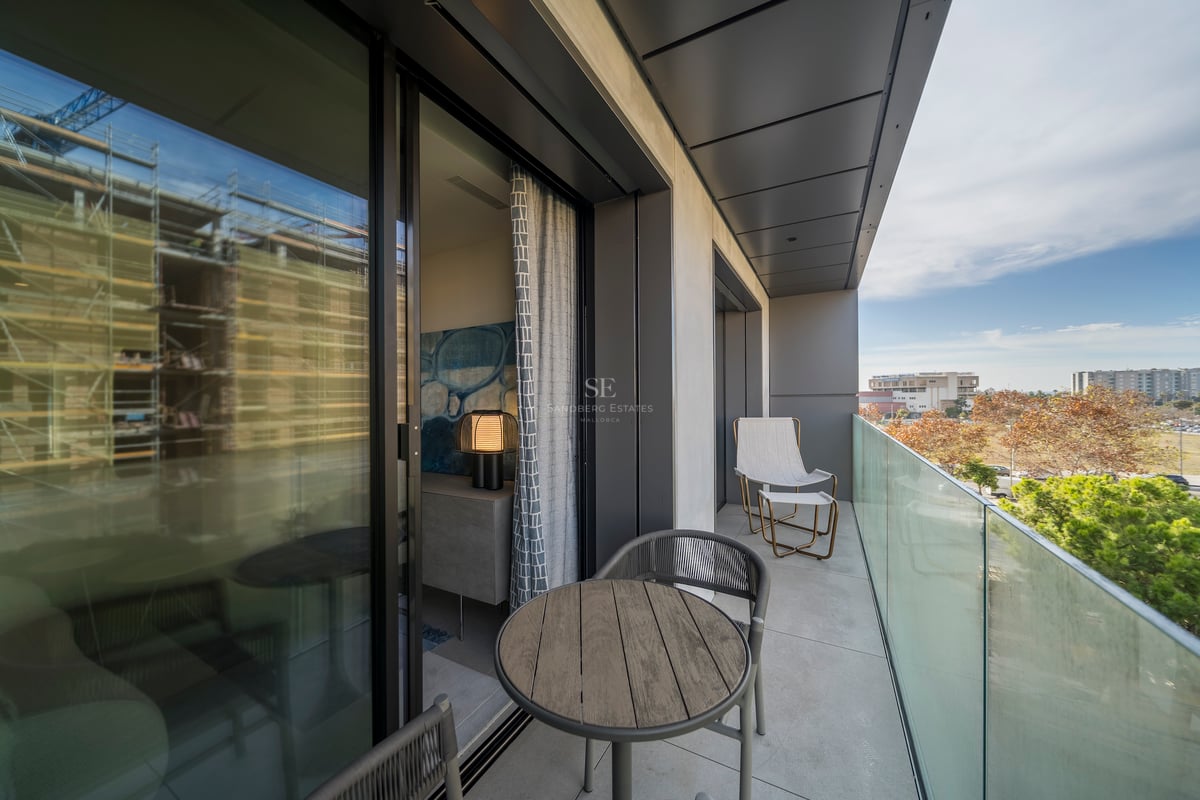 Balcon contemporain avec garde-corps en verre, table en bois et sièges donnant sur un parc.