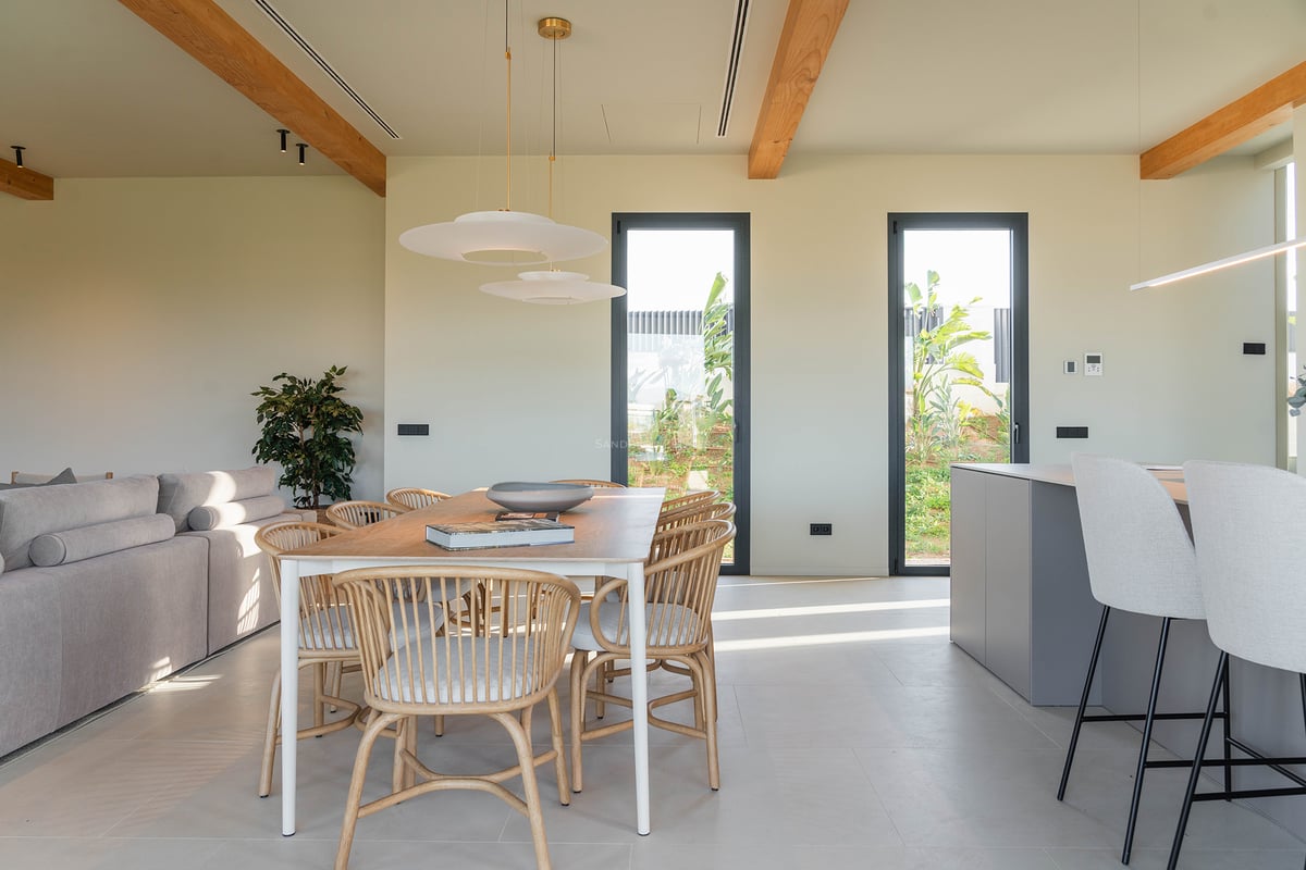 Lichtdurchflutetes Esszimmer mit Holztisch, Designerstühlen und sichtbaren Deckenbalken.