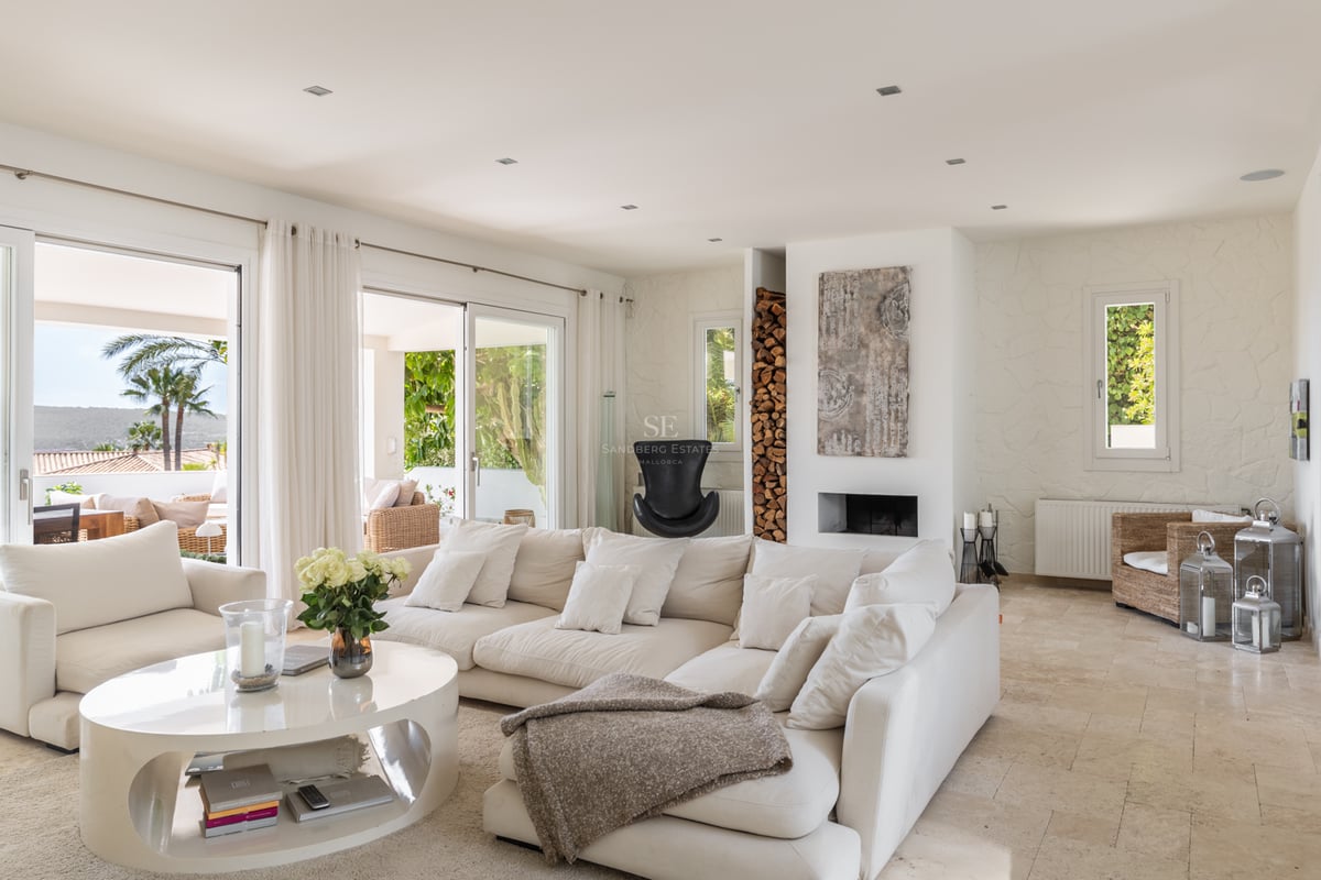 Grand salon aux tons crème avec sol en travertin et baies vitrées ouvrant sur une terrasse ensoleillée.