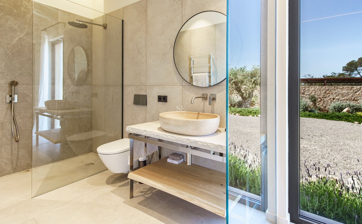 Baño contemporáneo con lavabo de piedra natural sobre encimera, espejo circular y ducha a ras de suelo.