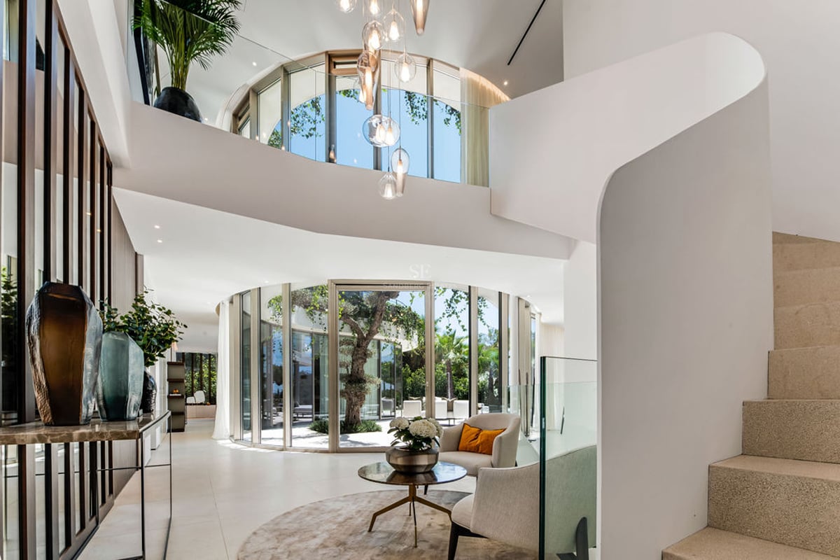 Entrée de luxe avec parois de verre courbes, patio central, escalier blanc sculptural et sol en pierre naturelle.