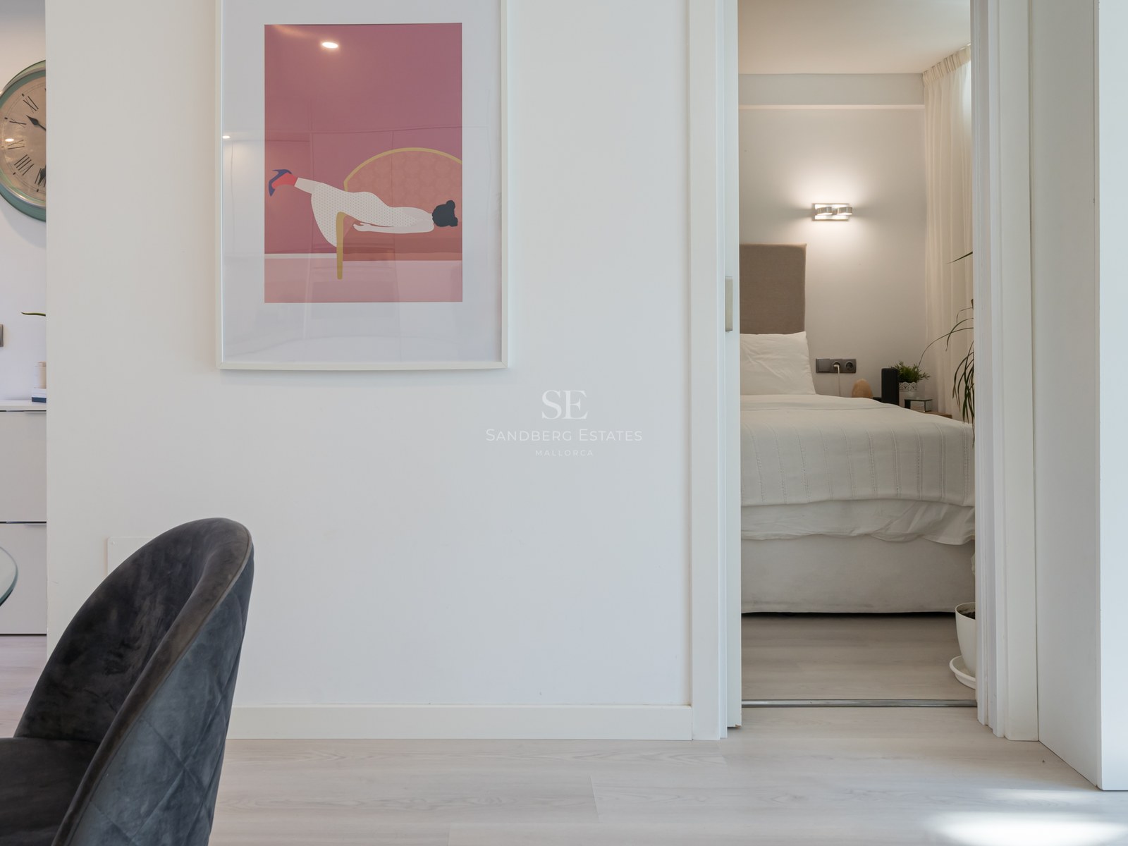 Vue à travers une porte ouverte sur une chambre minimaliste avec un grand lit, tête de lit beige et éclairage tamisé.