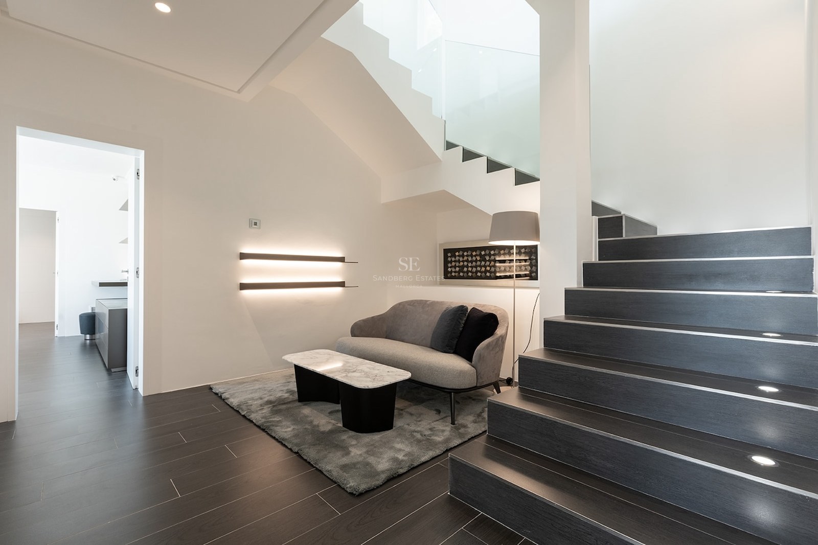 Modern interior featuring dark stairs with integrated LED lighting, a gray sofa, and a marble coffee table.