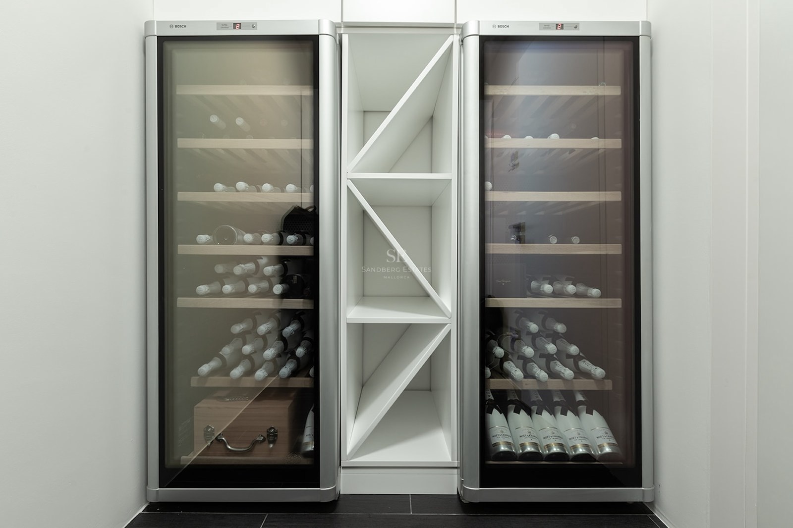 Two sleek silver Bosch wine fridges flanking a central white geometric bottle rack in a minimalist interior.