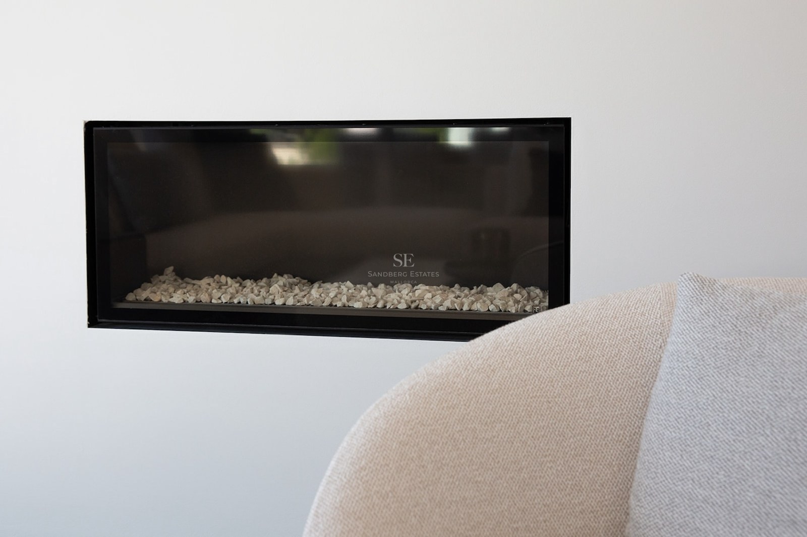 Close-up of a rectangular black-framed fireplace built into a white wall with white stones inside.