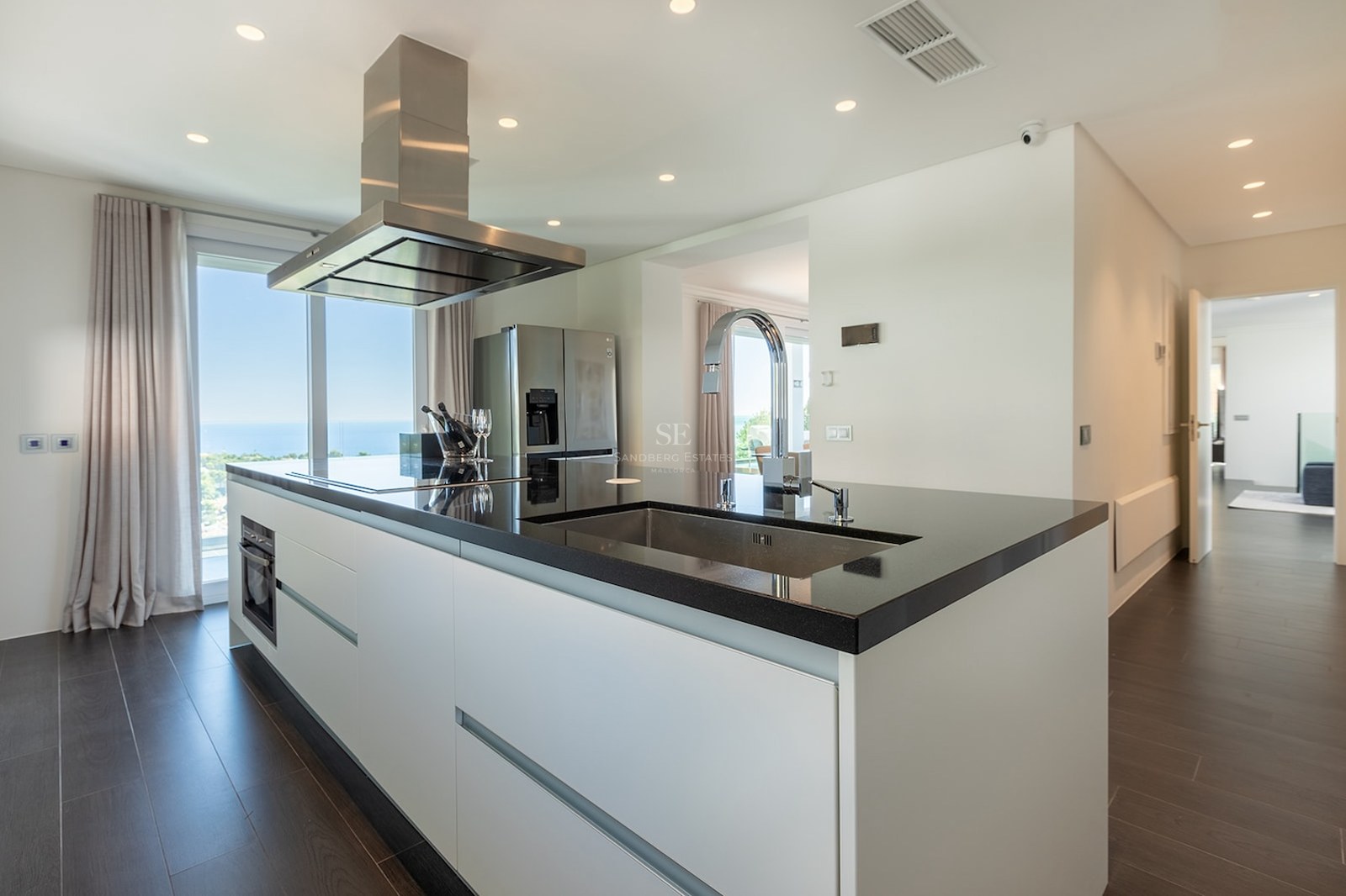 Modern kitchen featuring a black island, stainless steel hood, and floor-to-ceiling windows with a sea view.