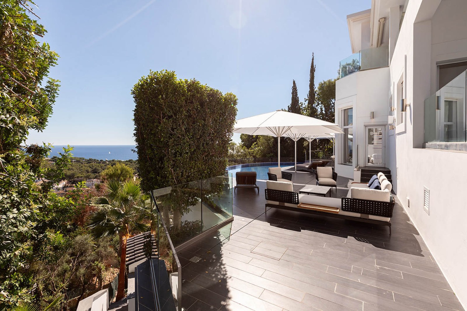 Modern terrace with designer lounge furniture, white umbrellas, and an infinity pool overlooking the sea.