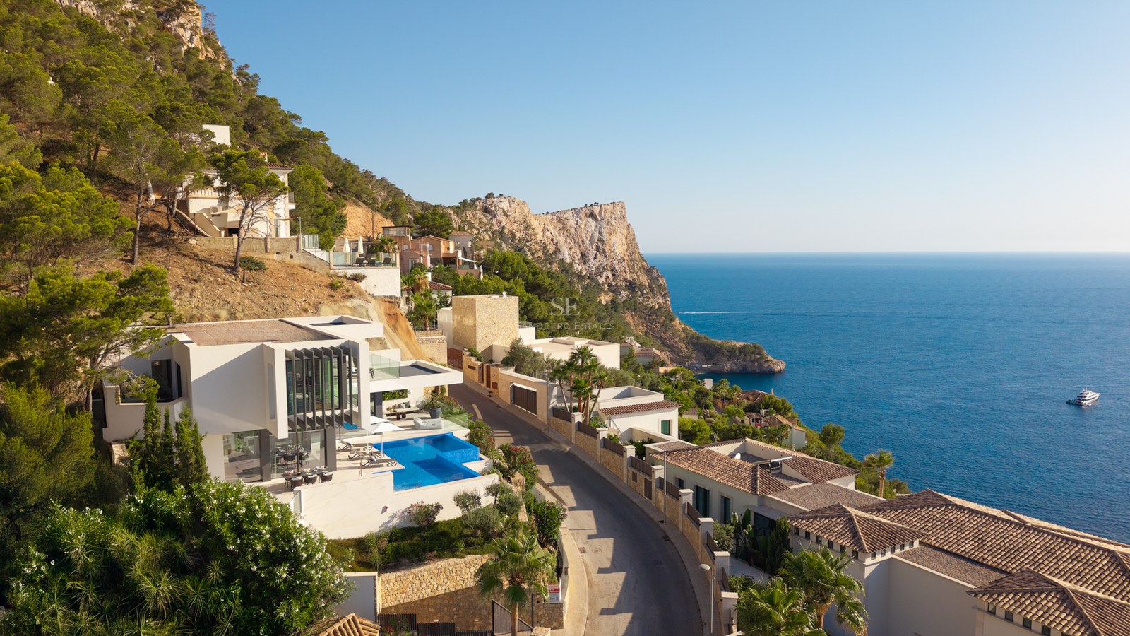 Aerial view of a white modern villa with an infinity pool on a cliffside overlooking the blue Mediterranean sea.