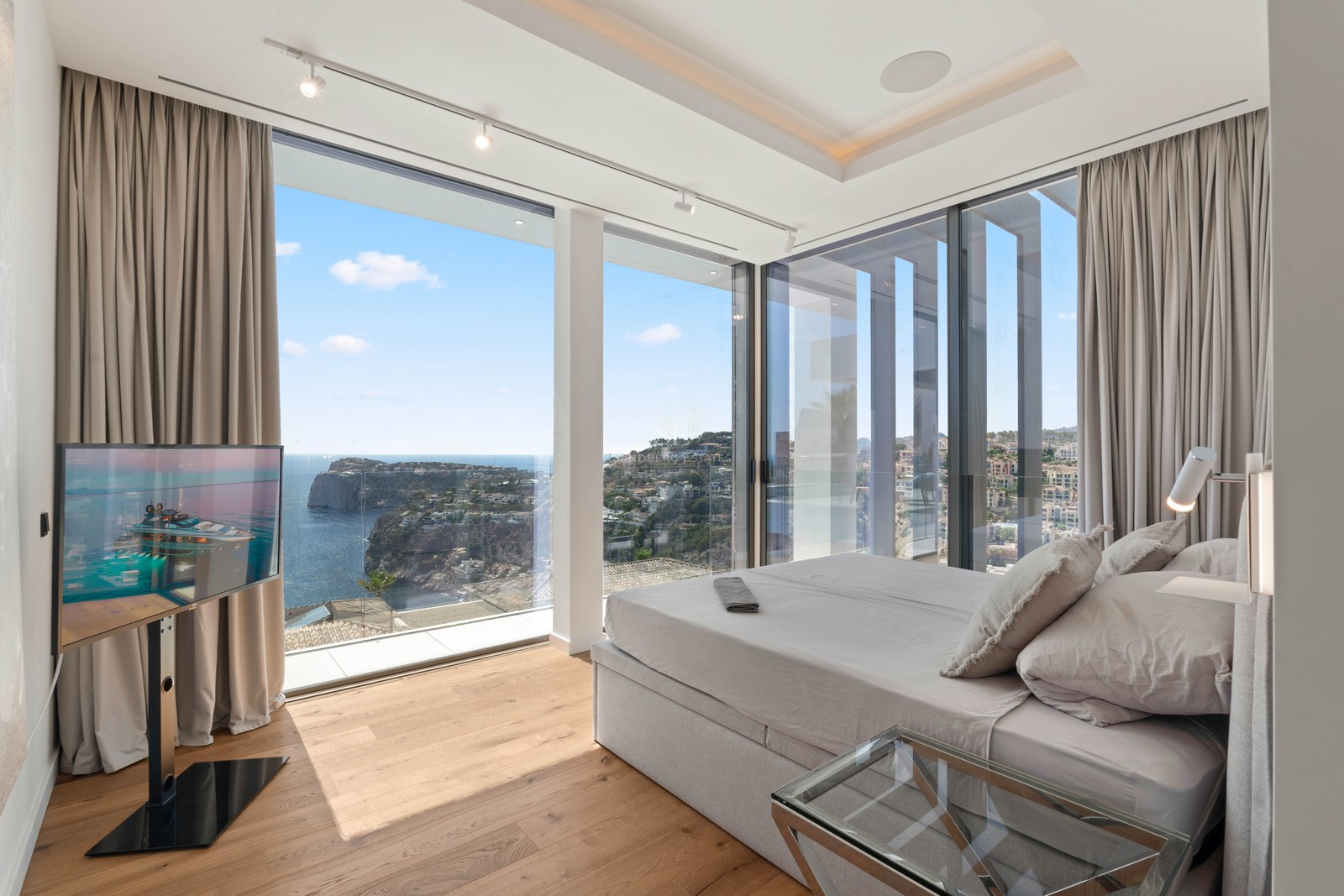 Modern bedroom with floor-to-ceiling windows showing a panoramic view of the sea and coastline.