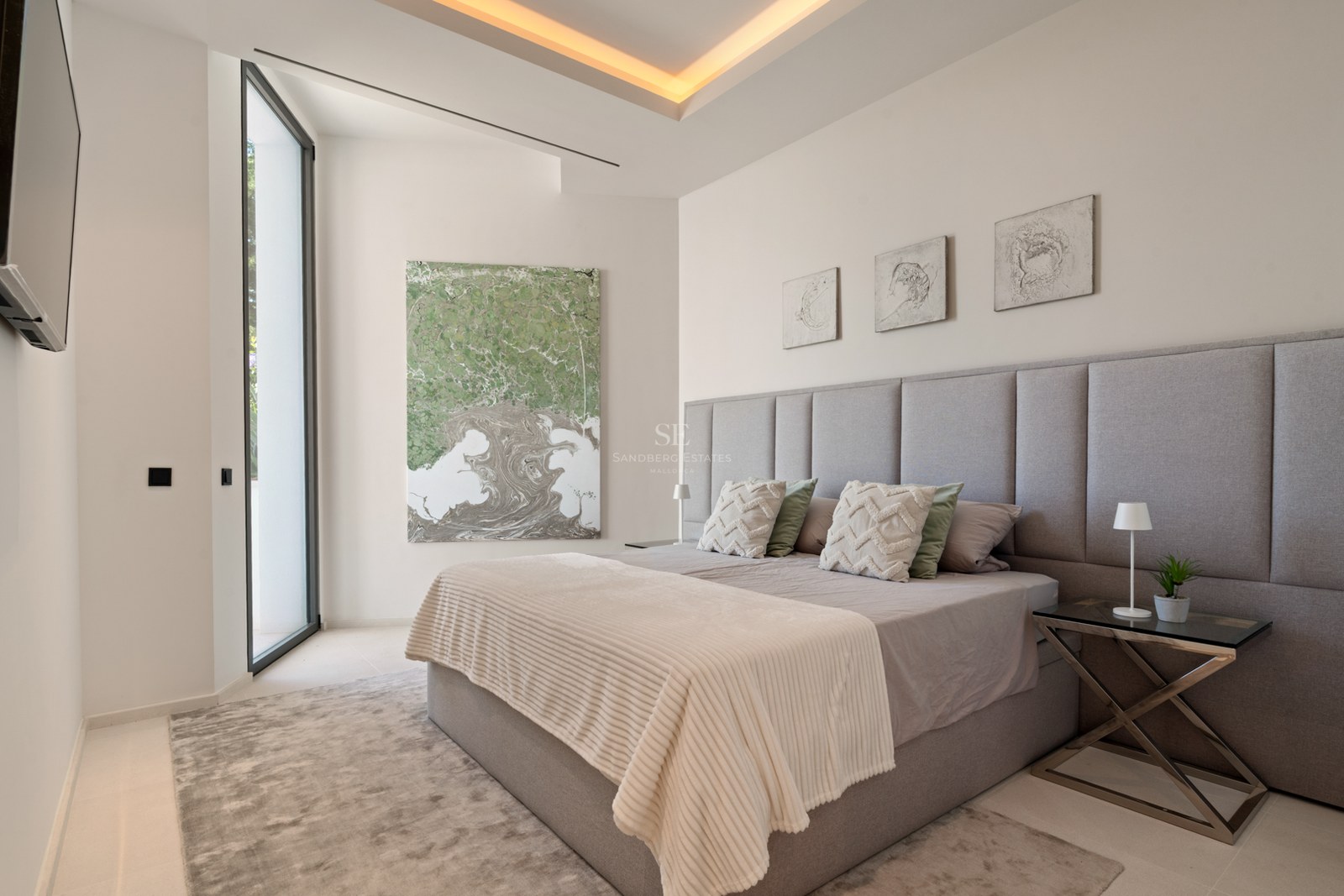 Bedroom with grey upholstered headboard, king-size bed, abstract art, and warm recessed lighting.