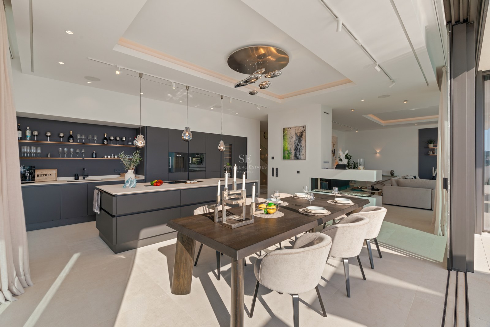 Modern dining area with dark wood table, beige chairs, and sleek gray kitchen featuring floor-to-ceiling windows.