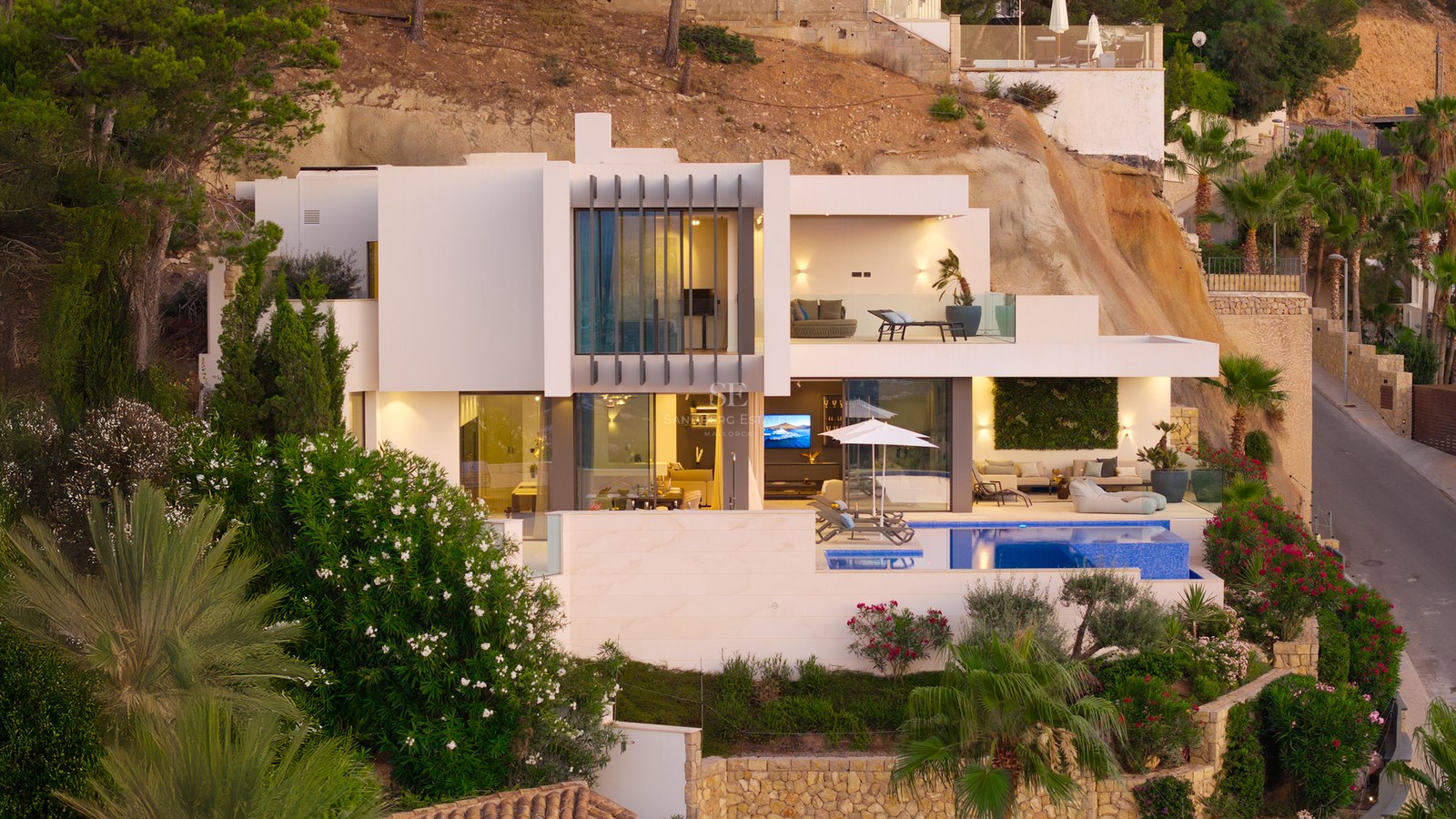 Modern white multi-level villa with a swimming pool, terraces, and large glass windows built into a rocky hillside.