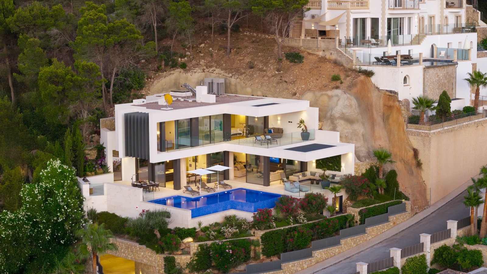 Modern white villa on a hillside featuring a bright blue swimming pool and glass-walled terraces.