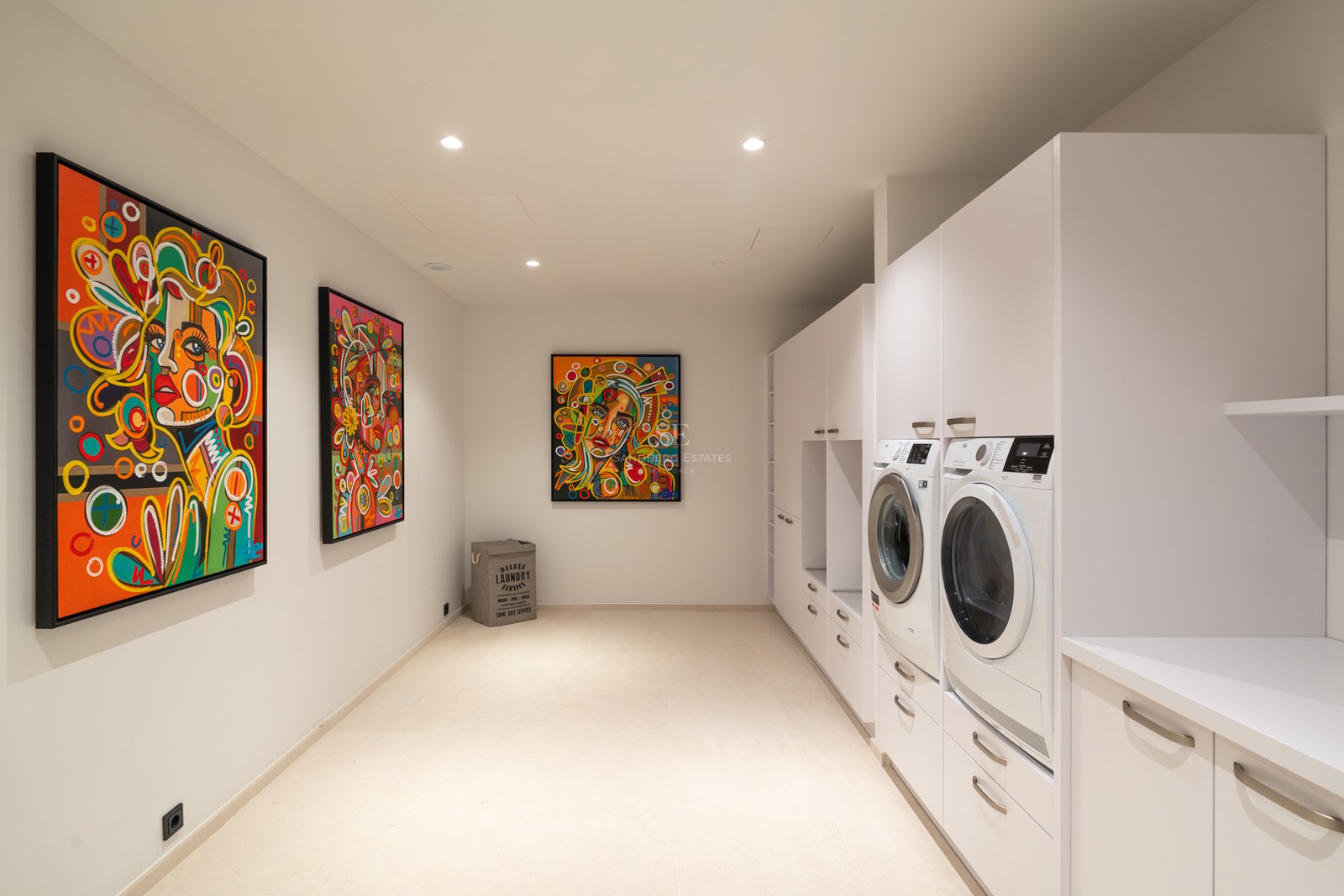 Modern white laundry room with washer, dryer, minimalist cabinetry, and three vibrant colorful pop-art portraits.