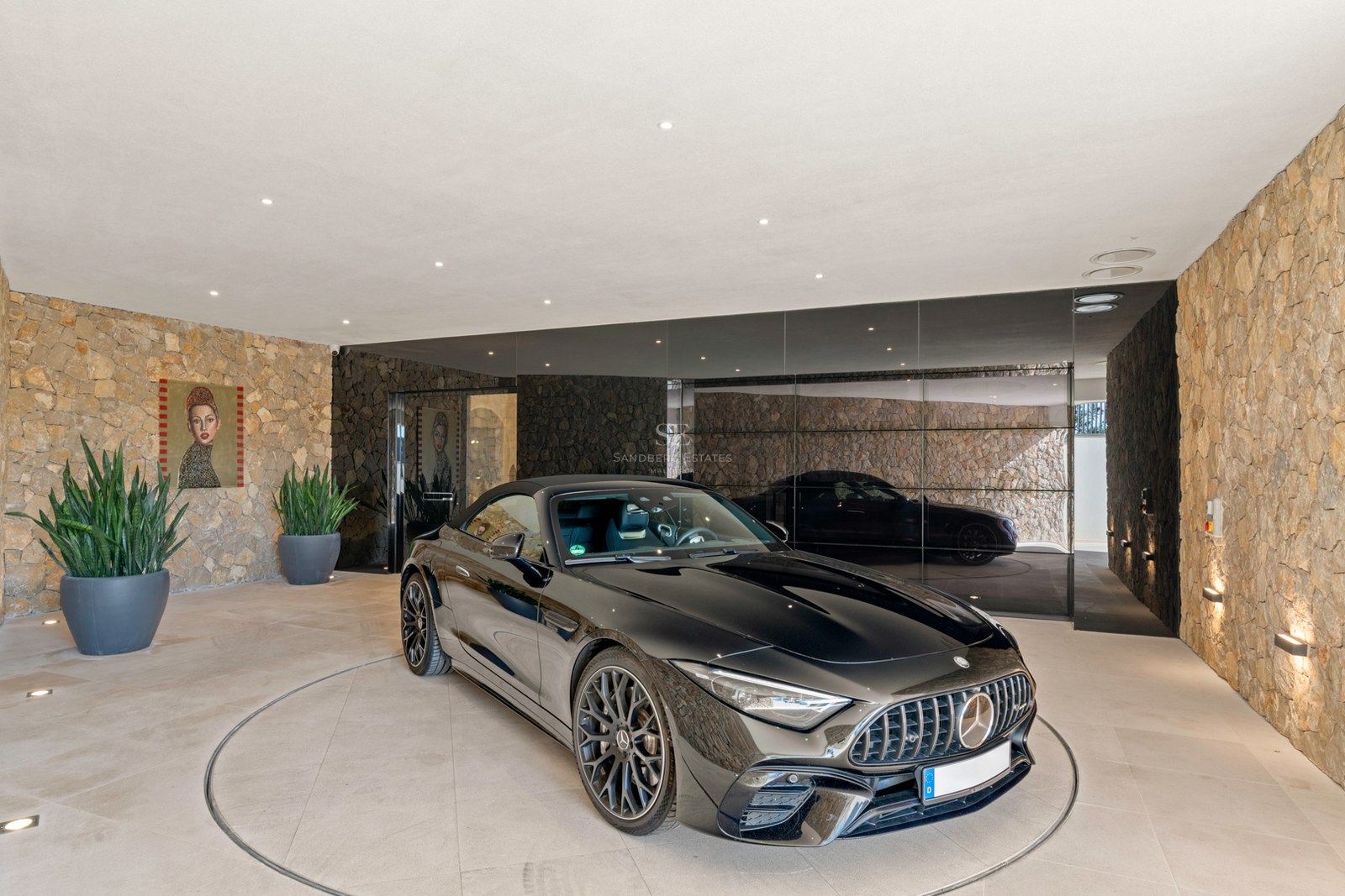 A black Mercedes sports car on a circular rotating platform in a modern garage with natural stone walls and mirrors.