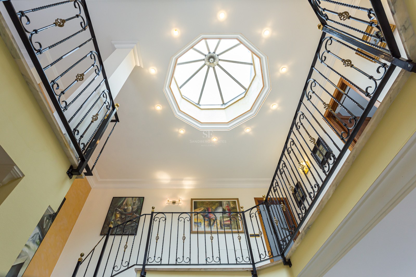 Upward view of a grand staircase with wrought iron railings and a large octagonal skylight in the ceiling.