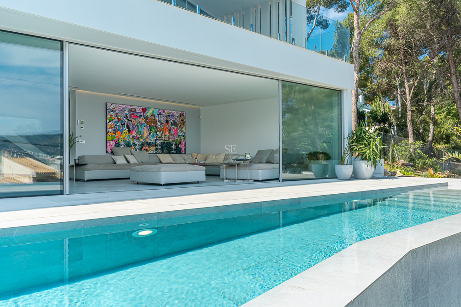 A crystal-clear pool in front of a modern open-plan living room with large glass sliding doors and pop art.