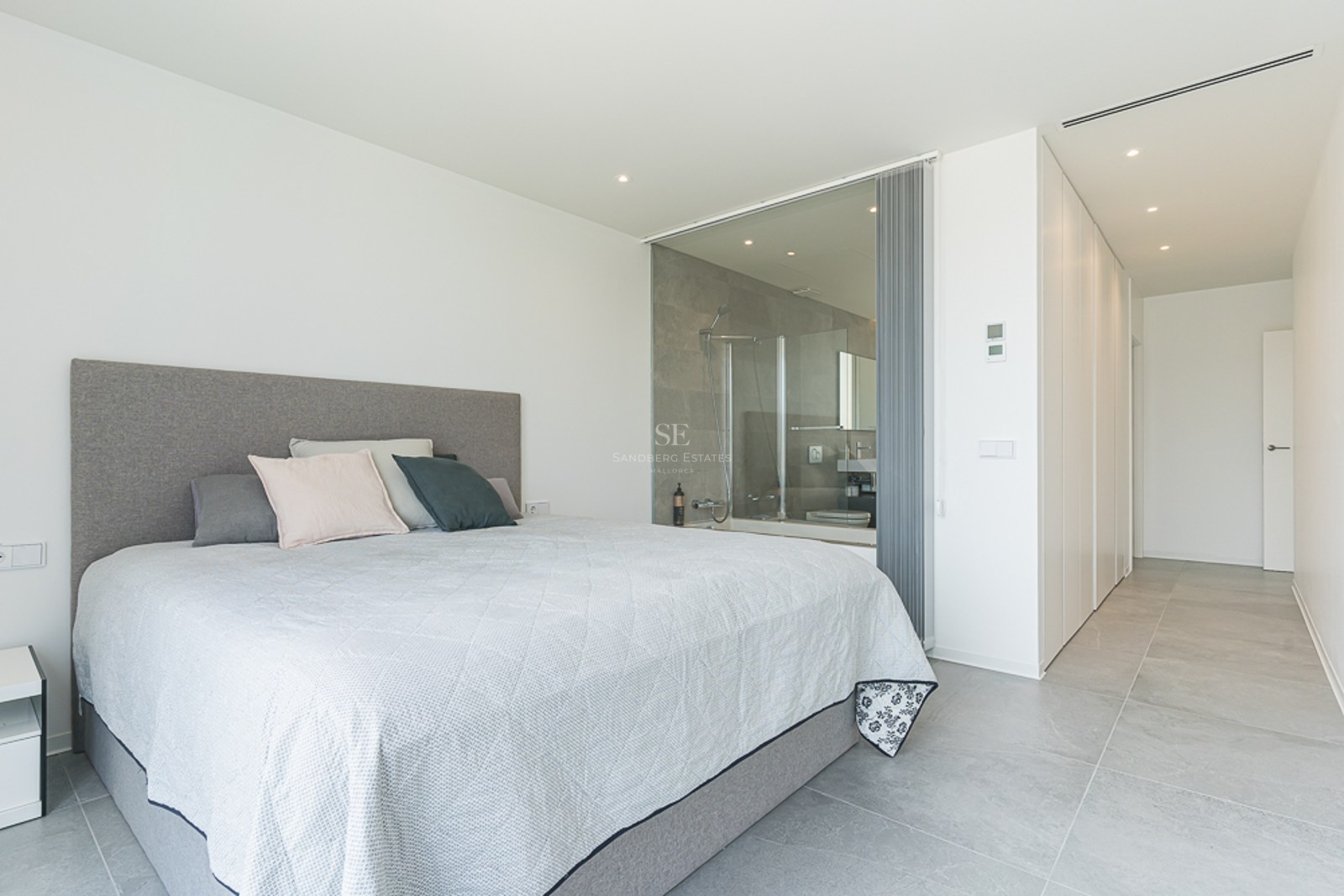 Minimalist master bedroom with a large bed and a glass-enclosed ensuite bathroom featuring a walk-in shower.