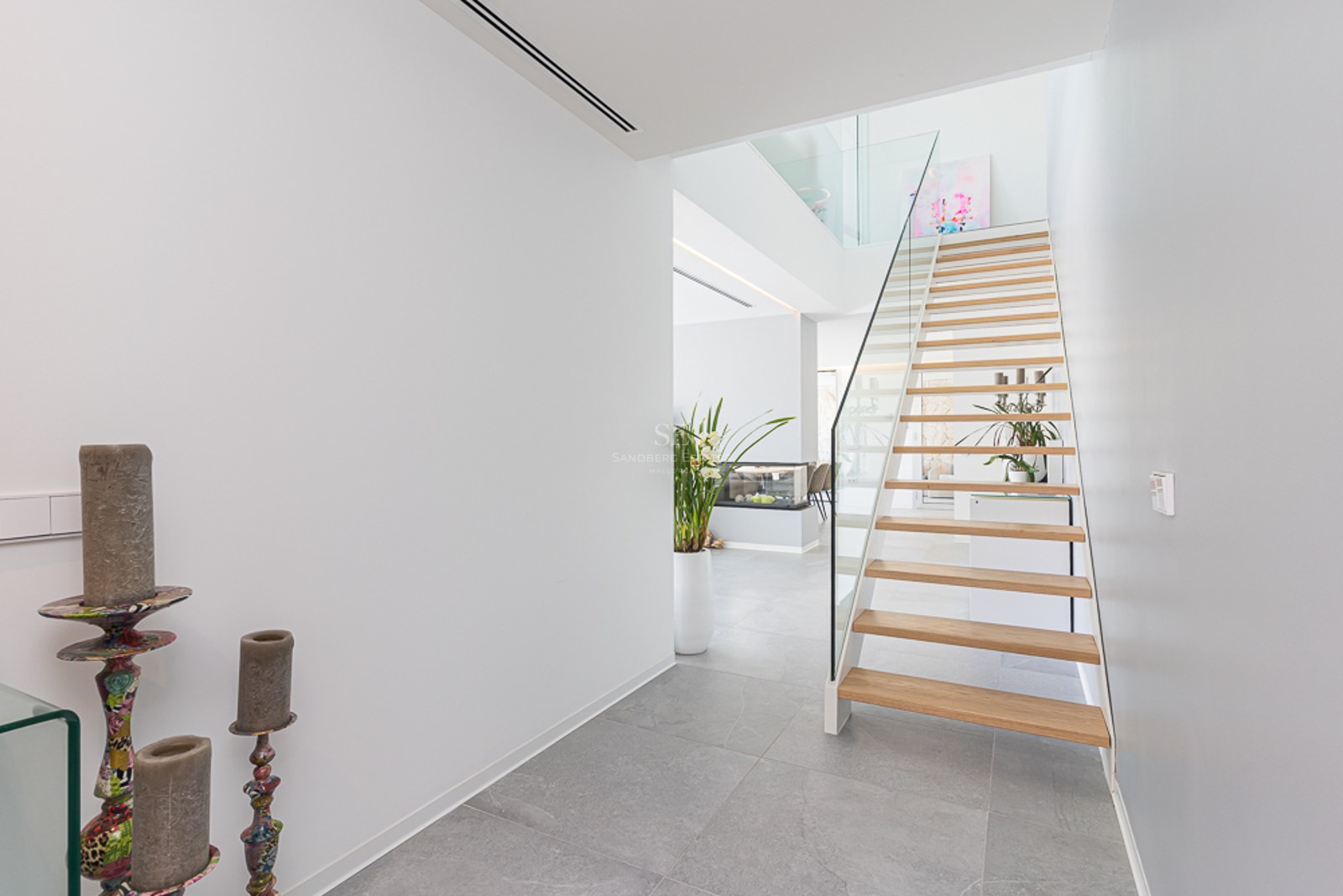 Bright modern hallway featuring a light wood floating staircase with glass railings and grey stone flooring.