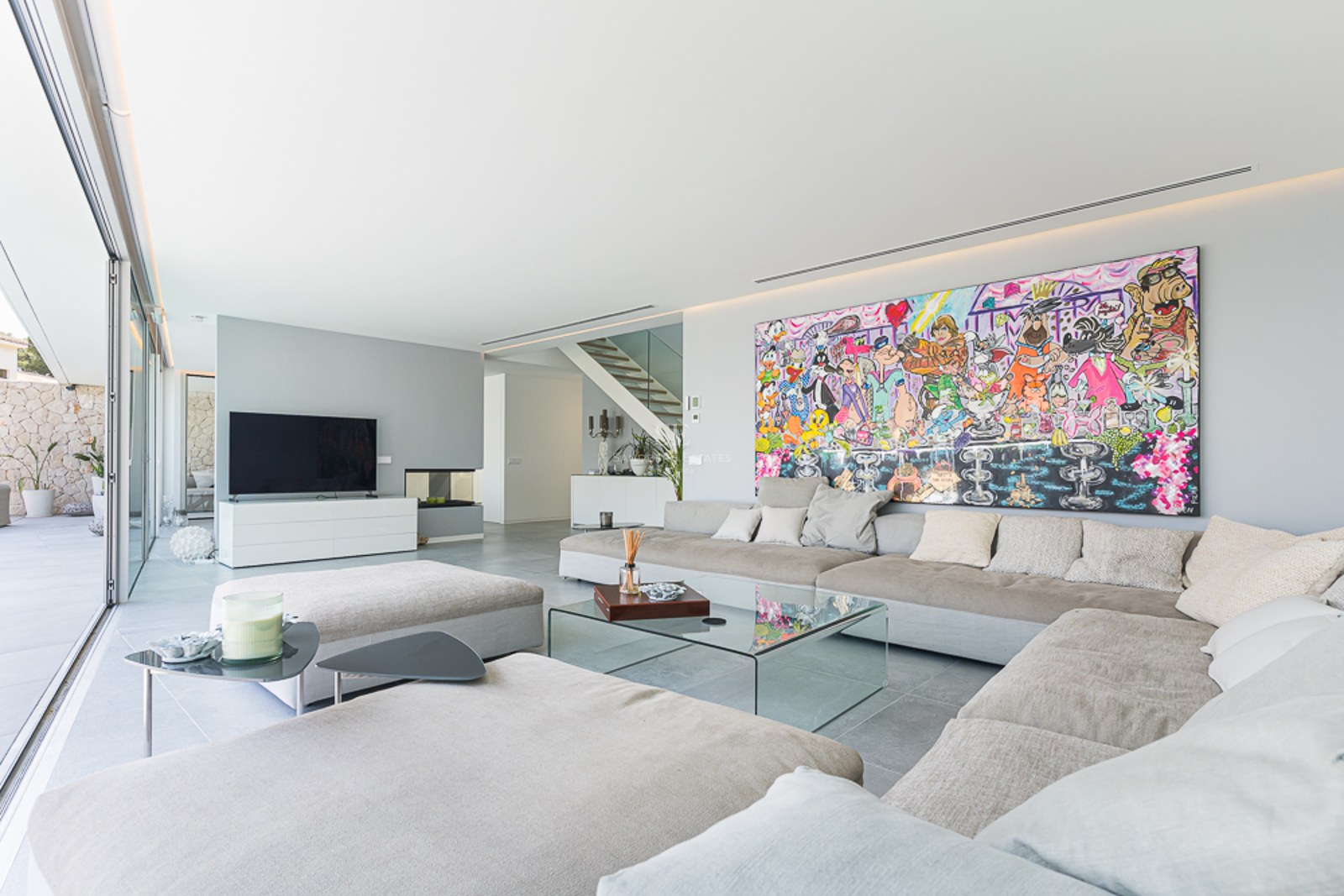 Modern living room with large beige sofa, glass table, and a massive colorful cartoon painting on a white wall.