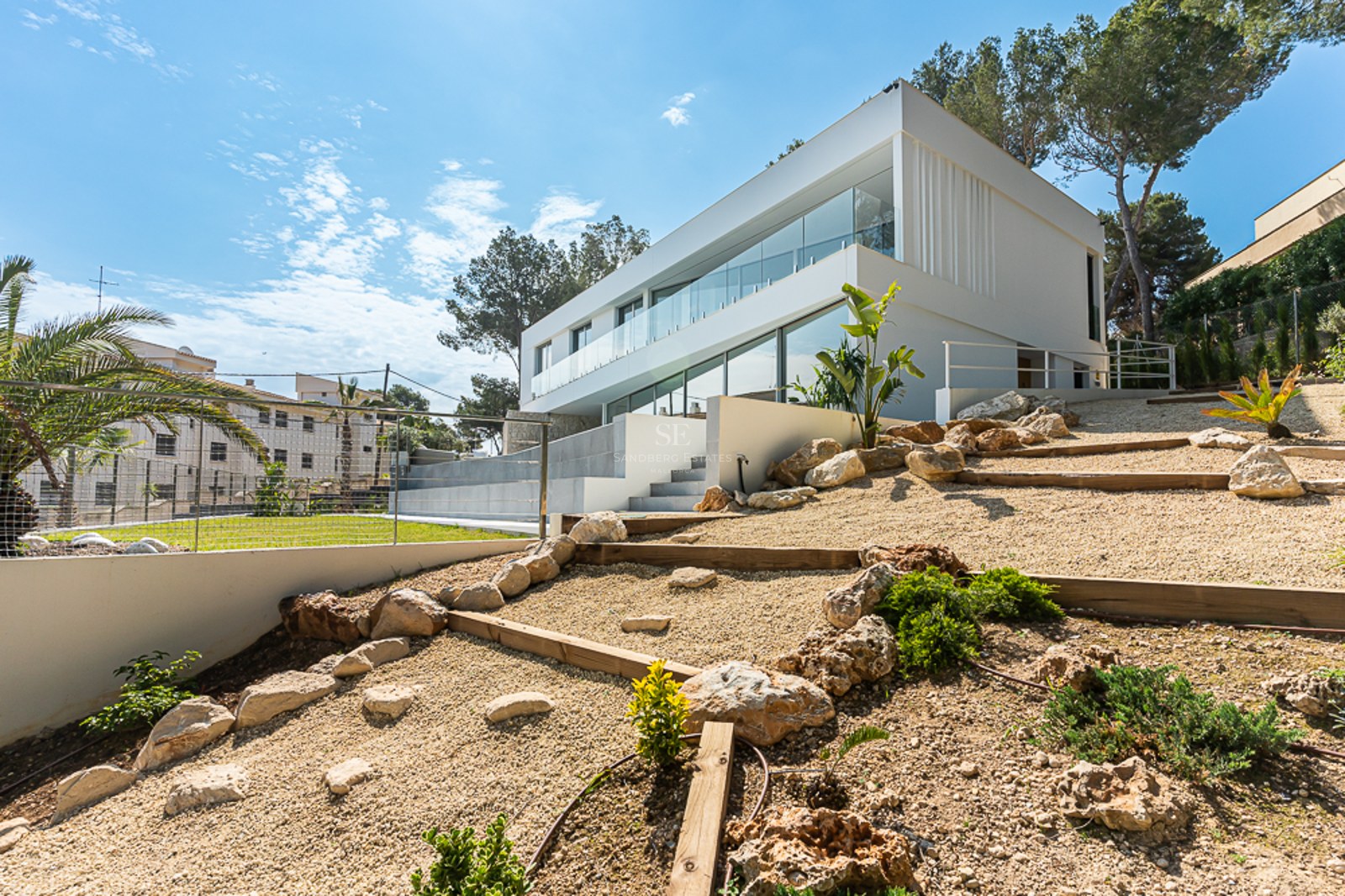 Side view of a modern two-story white villa with large glass windows and a tiered rock garden with gravel.