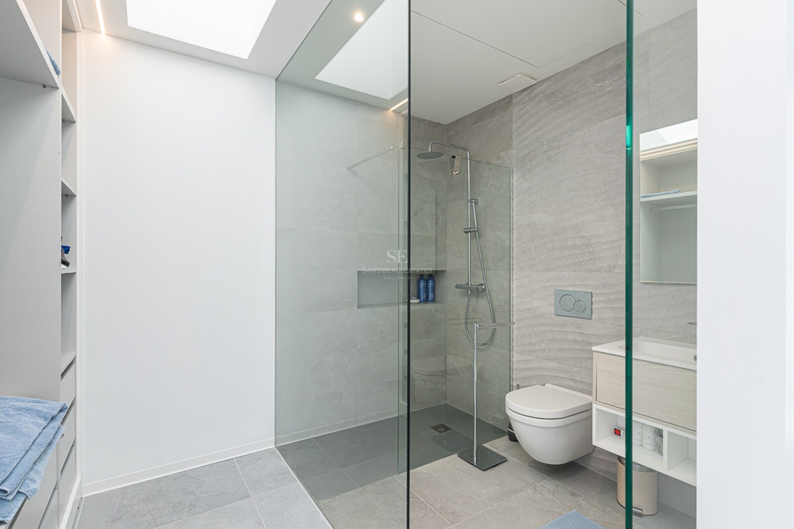 Minimalist bathroom featuring grey stone tiles, a glass walk-in shower, wall-hung toilet, and a bright skylight.