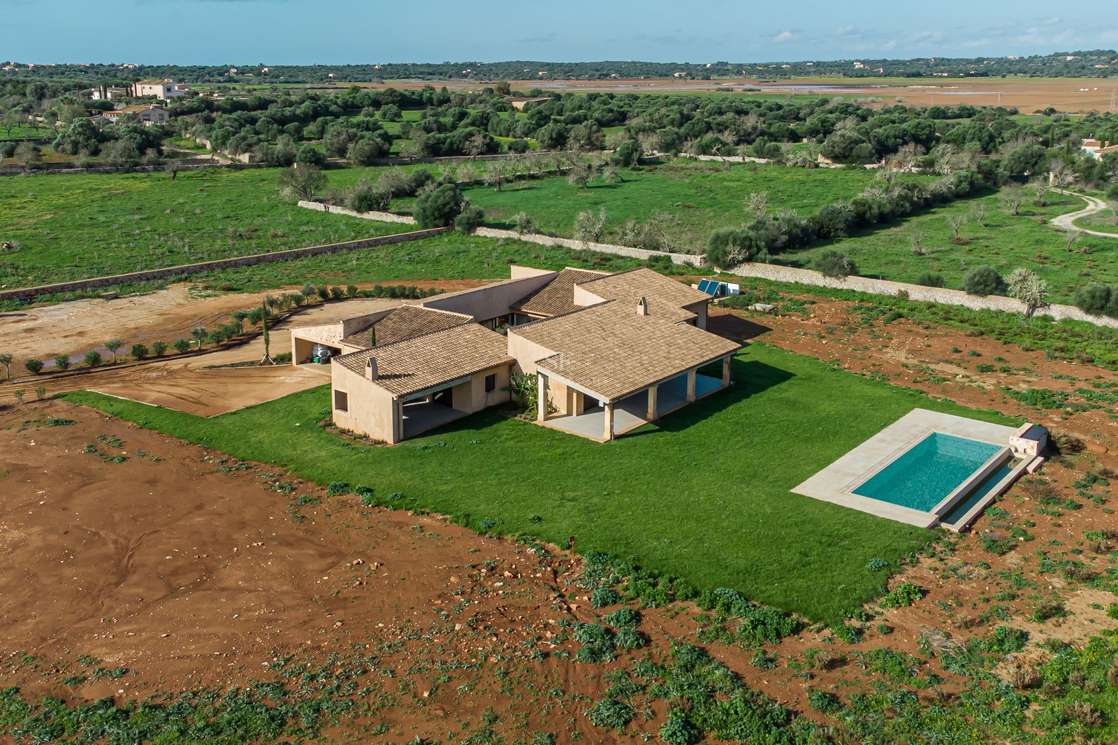 Bird's eye view of a sand-colored modern villa with a turquoise pool and large lawn in a rural landscape.
