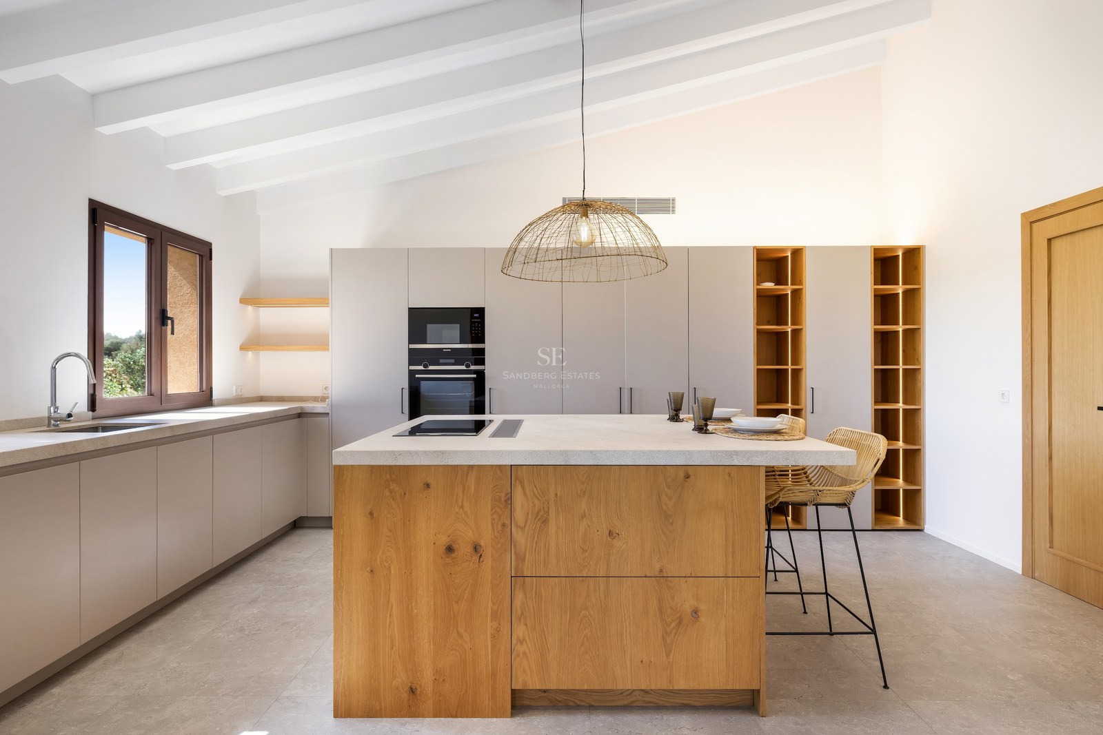 Bright kitchen featuring a large oak island, white beamed ceiling, and integrated lighting in open shelving.