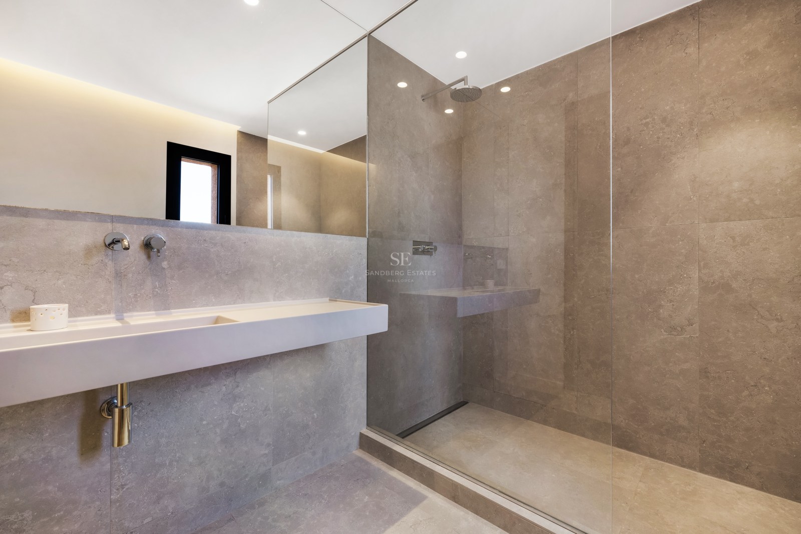 Minimalist bathroom with gray stone tiles, glass walk-in shower, wall-mounted sink, and large mirror.