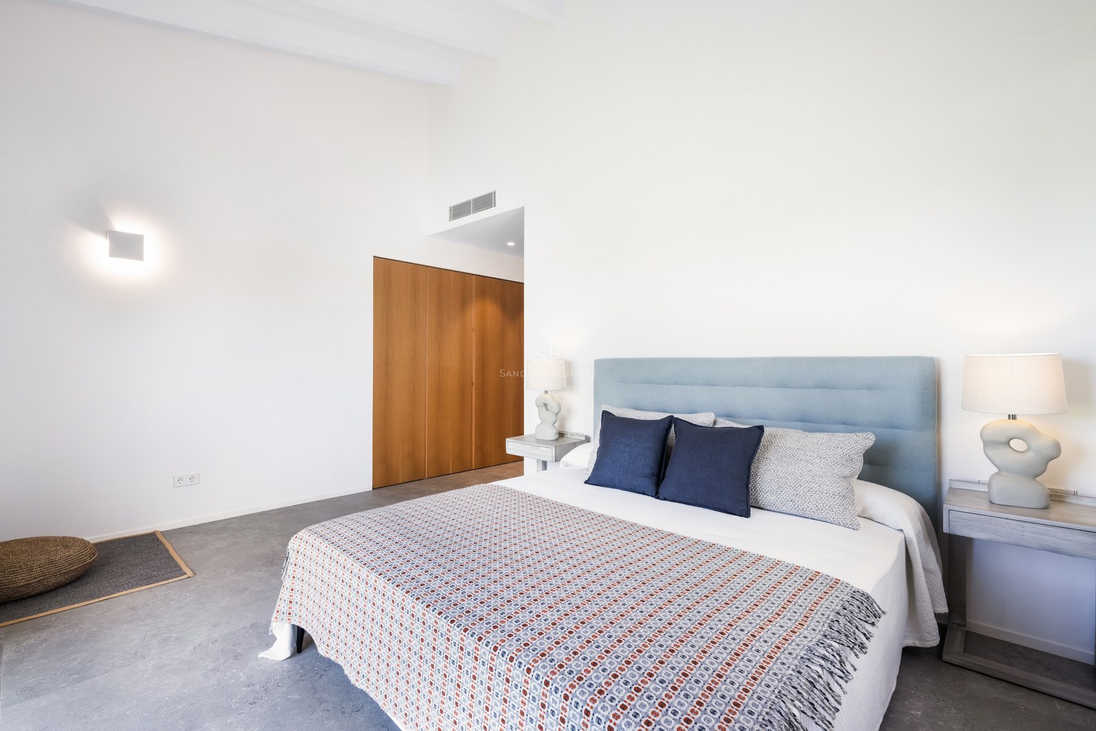 Bright bedroom with a large bed, light blue headboard, designer lamps, and built-in wooden wardrobe.
