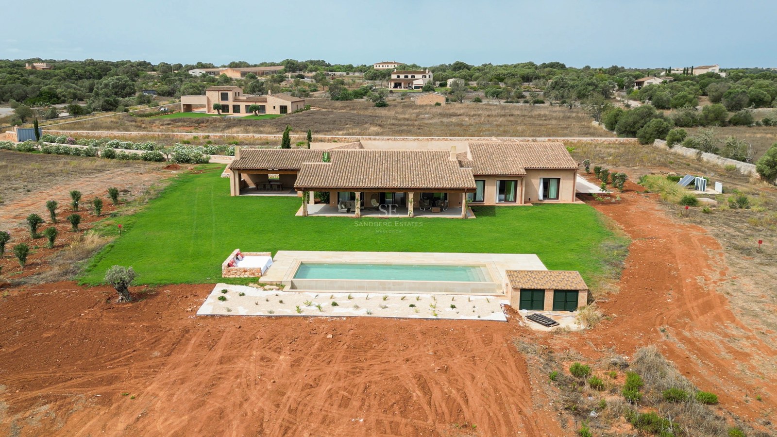 Bird's eye view of a luxury villa with terracotta roof, rectangular swimming pool, and large green lawn.