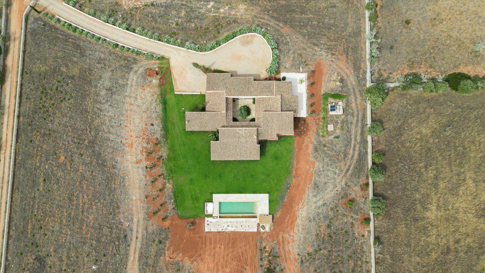 Top-down drone view of a tiled-roof villa with a central interior courtyard, lawn, and rectangular swimming pool.