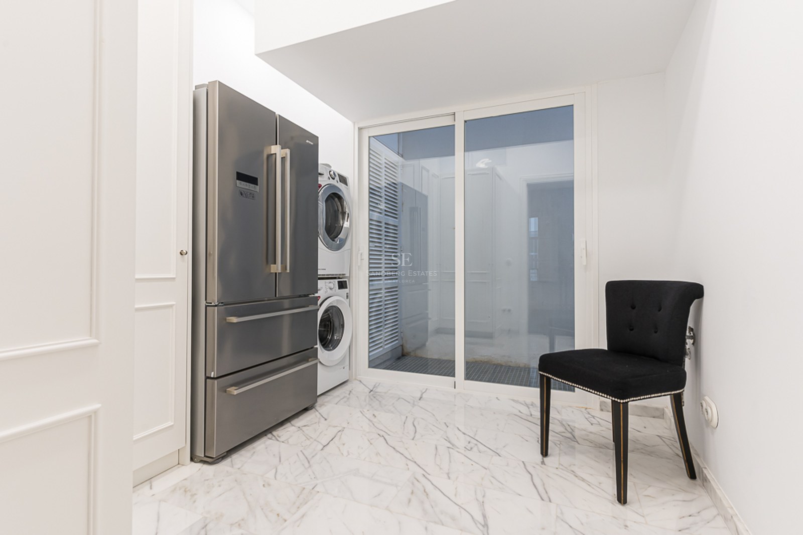 Utility room featuring a stainless steel refrigerator, stacked laundry unit, and white marble flooring.