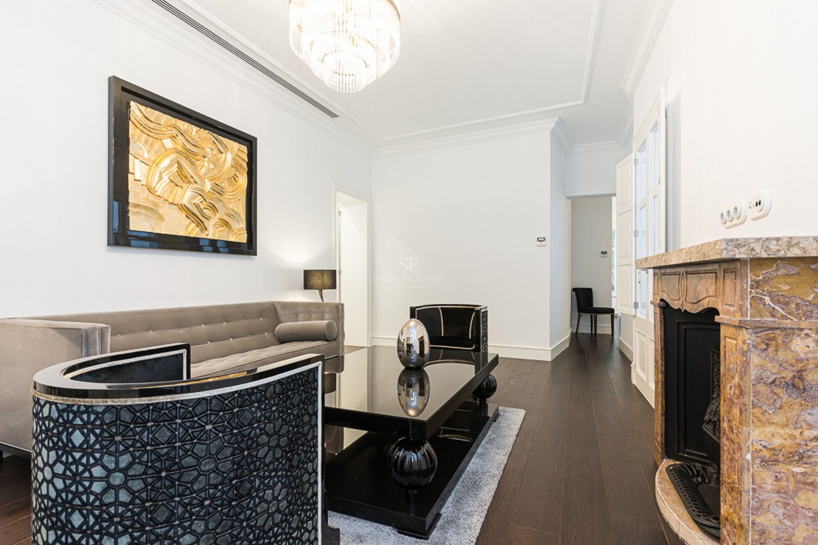 Luxury living room with grey velvet sofa, black table, marble fireplace, and gold wall art.