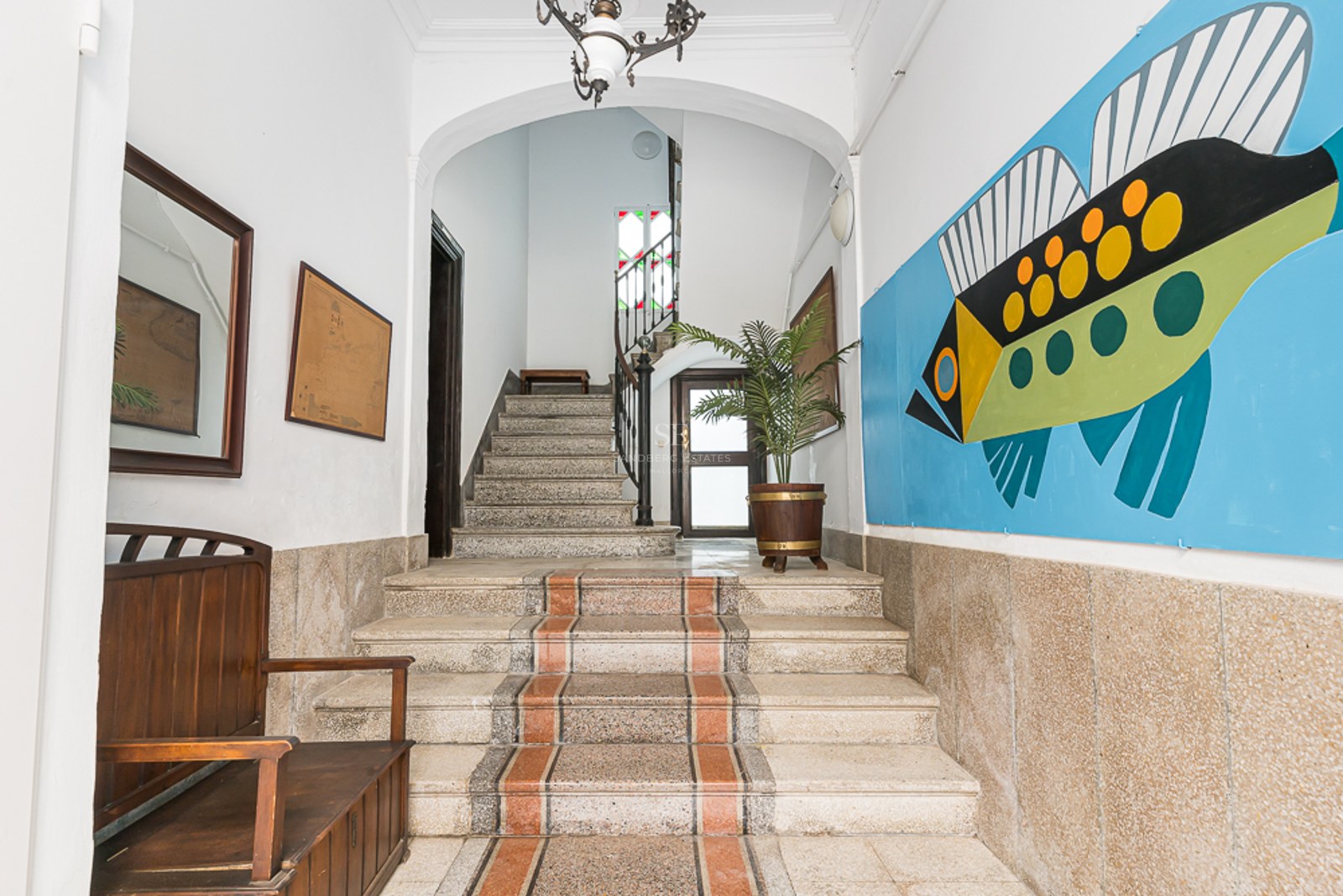 Entrance with stone stairs, wooden bench, and a large colorful fish mural on the wall.