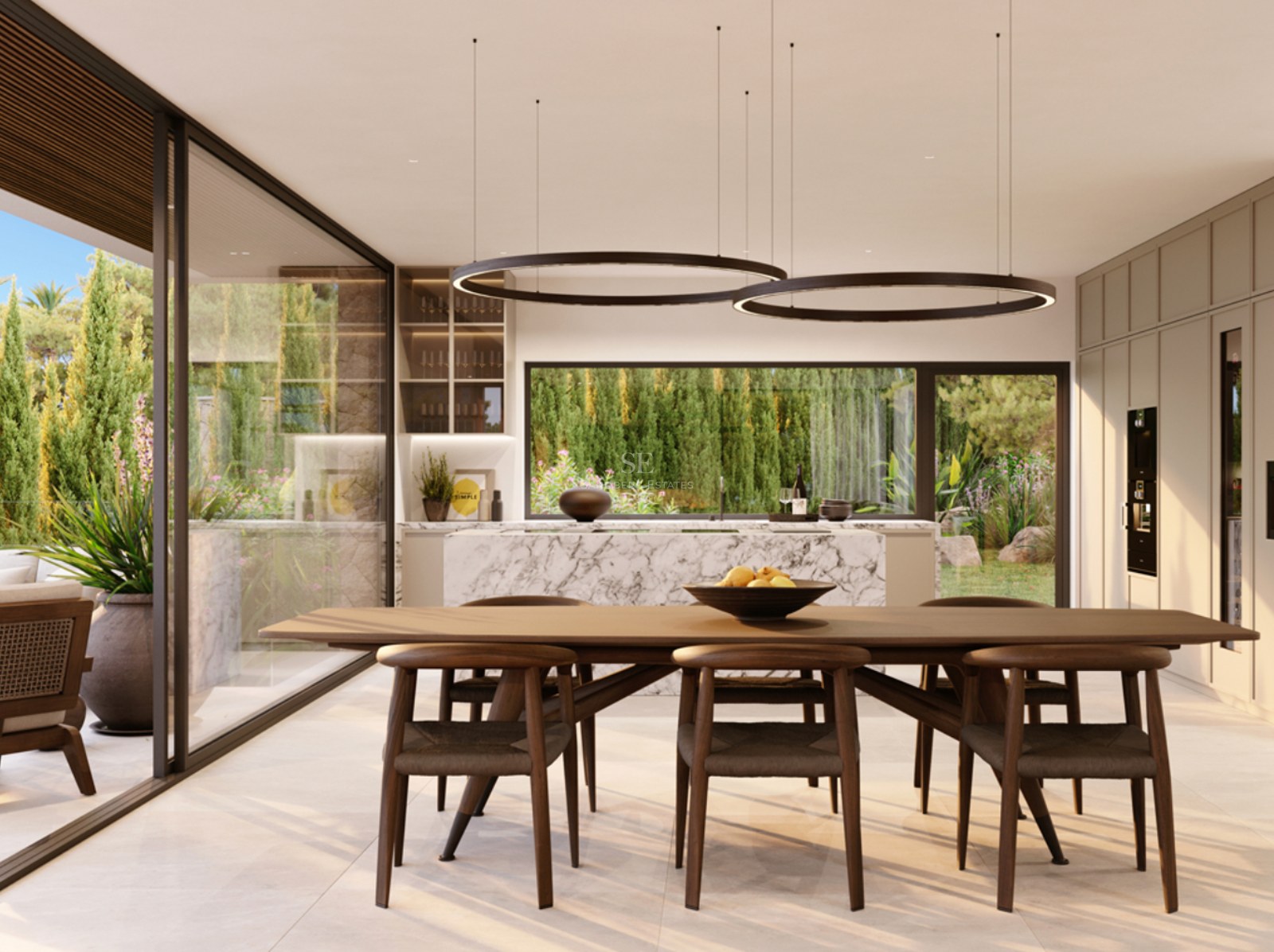 A sleek wooden dining table with chairs under circular pendant lights, overlooking a marble kitchen and lush garden.